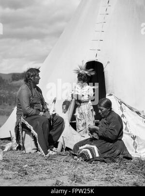 1920s NATIVE AMERICAN INDIAN FAMILY MAN WOMAN CHILD BY TEPEE STONEY SIOUX TRIBE NEAR ALBERTA CANADA Stock Photo