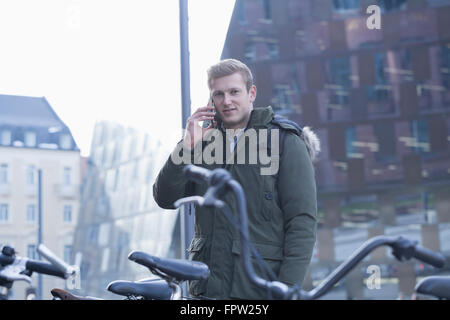 Young student standing outside parking lot with bicycle and talking on mobile phone, Baden-Württemberg, Germany Stock Photo