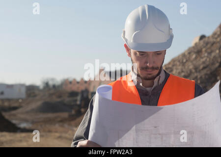 Young male engineer holding blueprint at construction site, Freiburg Im Breisgau, Baden-Württemberg, Germany Stock Photo
