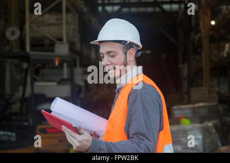 Young male engineer holding blueprint and using digital tablet at construction site, , Baden-Württemberg, Germany Stock Photo