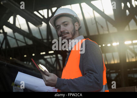 Portrait of an engineer holding blueprint and using digital tablet at construction site, Baden-Württemberg, Germany Stock Photo