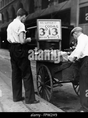 1930s YOUNG MAN CUSTOMER AND SIDEWALK STREET VENDER WITH HANDCART SELLING SODAS FOR 3 CENTS & 5 CENTS FOR PEPSI COLA Stock Photo