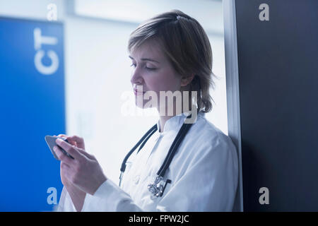 Young female doctor text messaging on mobile phone in clinic, Freiburg im Breisgau, Baden-Württemberg, Germany Stock Photo