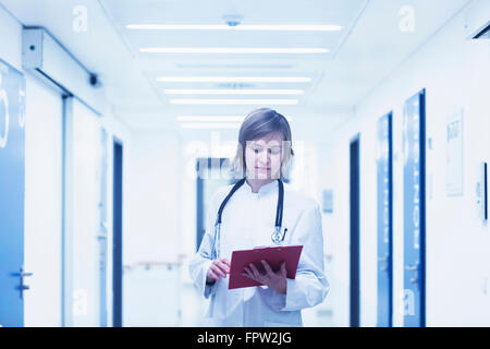 Young female doctor holding clipboard in hospital corridor, Freiburg im breisgau, Baden-Württemberg, Germany Stock Photo
