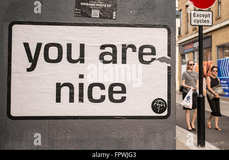 White billboard with the words 'You are nice' on a wall in a street in London. Two woman with sunglasses walking next to it. Stock Photo