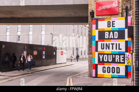 Two hipster girls walking next to a big colored billboard with the words 'Be bad until you're good' on it. Stock Photo