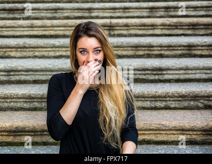 Beautiful woman with long hair covering her mouth in shock while staring at camera with astonishment Stock Photo