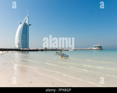 Woman with surf board on Jumeirah Beach with Burj al Arab hotel in the background, Dubai, United Arab Emirates Stock Photo