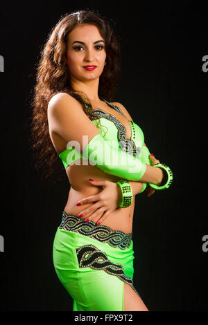 beautiful young brunette in a green suit oriental dance on black background Stock Photo