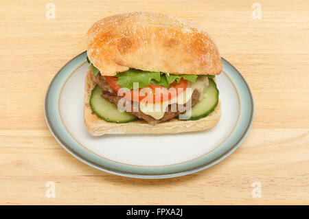 Cheeseburger with salad in a ciabatta roll on a plate on a wooden tabletop Stock Photo