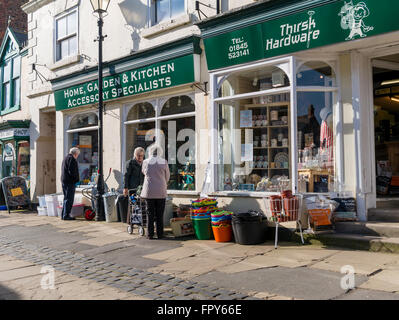 Women talking outside outside a hardware shop with goods displayed in a pedestrianised area of Thirsk Market Place Yorkshire Stock Photo