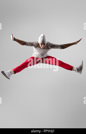 One young urban style breakdancer guy in casual red pants and beanie working out, dancing and jumping. Full length photo on stud Stock Photo