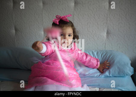 Little girl costumed as a fairy with magic wand sitting on the bed and playing Stock Photo