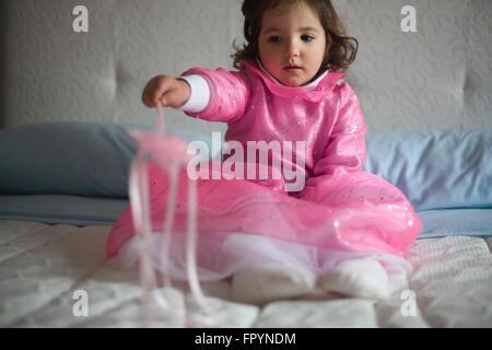 Little girl costumed as a fairy with magic wand sitting on the bed and playing Stock Photo