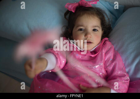 Little girl costumed as a fairy with magic wand sitting on the bed and playing Stock Photo