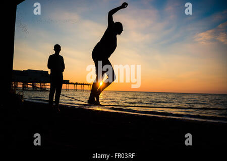Aberystwyth Wales UK, Sunday 20 March 2016   At then end of a day of unbroken sunshine in Aberystwyth on the west coast, a young couple practice slackline walking on the beach  the sun sets spectacularly behind them over Cardigan Bay    photo Credit:  Keith Morris / Alamy Live News Stock Photo