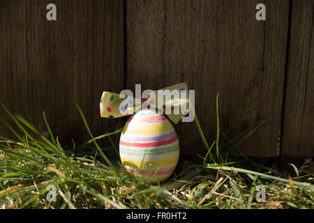 striped easter egg in the grass in front of a wood plank Stock Photo