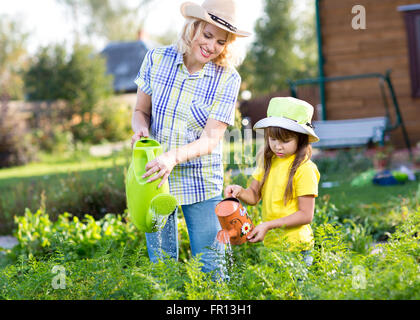 Woman with little girl watering plants in garden Stock Photo