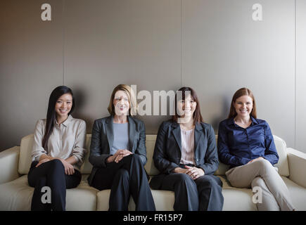Portrait smiling businesswomen sitting in a row on sofa Stock Photo