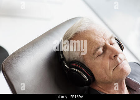 Senior man with headphones listening to music and reclining Stock Photo