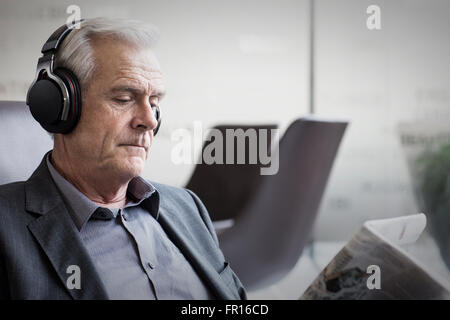 Senior businessman with headphones listening to music and reading newspaper Stock Photo