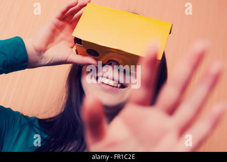 Brunette girl having fun playing with her cardboard virtual reality headset attached to her smartphone. Modern technology and vintage hipster colors Stock Photo