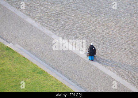 Aerial image of a lone woman with a stroller in a cobblestone square. Stock Photo