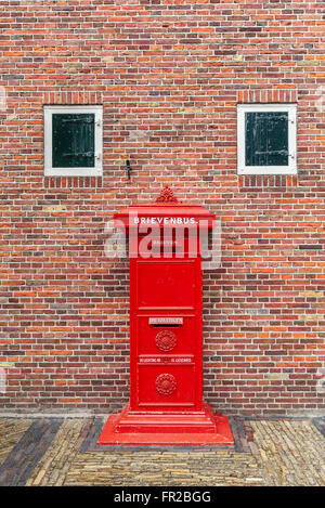 Old red postbox in front of brick wall in Zaanse Schans, Netherlands. Stock Photo