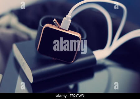 Smart wrist watch charging from a travel powerbank charger. Travel and stay connected to the media networks anywhere you want Stock Photo