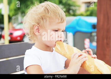 Outdoor closeup portrait of cute Caucasian blond baby girl eating French baguette Stock Photo