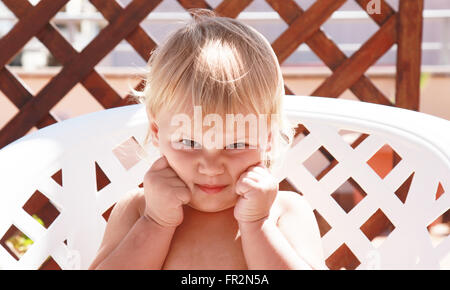 Small funny baby girl sitting in plastic armchair in a sunlight. Close-up outdoor portrait Stock Photo