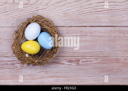 Three Easter colorful eggs in bird nest on wooden background Stock Photo