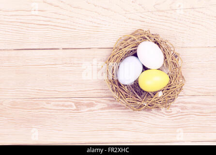 Three Easter colorful eggs in bird nest on wooden background Stock Photo