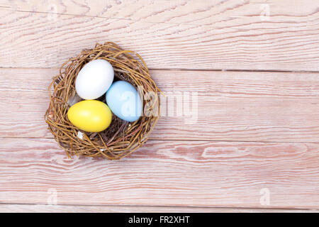 Three Easter colorful eggs in bird nest on wooden background Stock Photo