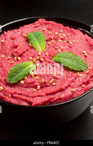 Beet hummus on a black bowl on black background Stock Photo
