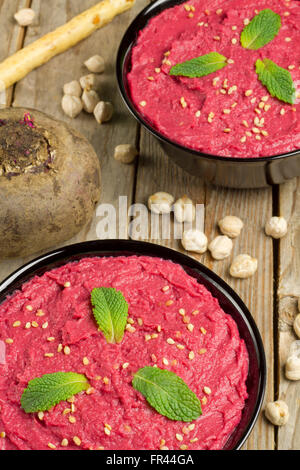 Beet hummus in two black bowls on a wooden table with ingredients Stock Photo