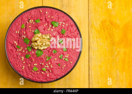 Beet hummus in a black bowl on a yellow wooden table Stock Photo