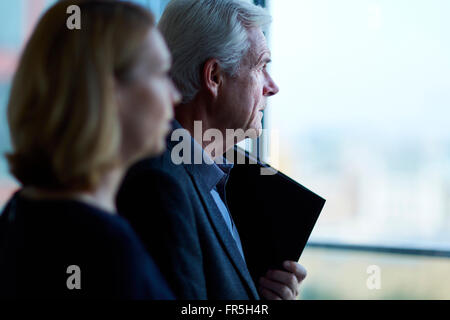 Pensive businessman and businesswoman looking through window Stock Photo