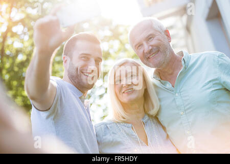 Smiling senior couple and adult son taking selfie outdoors Stock Photo