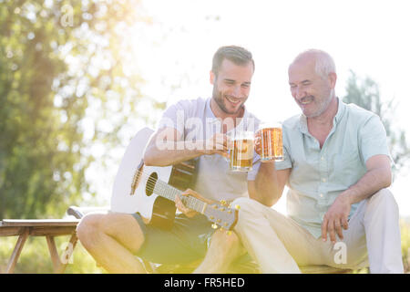 Father and adult son toasting beer mugs and playing guitar outdoors Stock Photo