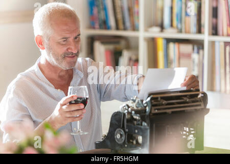 Senior man drinking wine at typewriter in study
