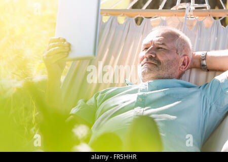 Senior man using digital tablet and relaxing in summer hammock Stock Photo
