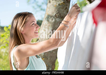 Smiling young woman hanging laundry on clothesline Stock Photo