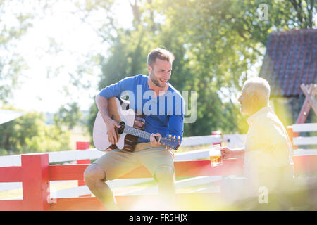 Father drinking beer and listening to adult son playing guitar Stock Photo
