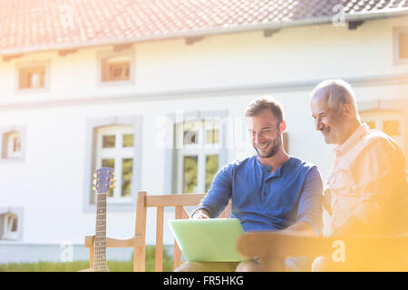 Father and adult son using laptop on garden bench Stock Photo