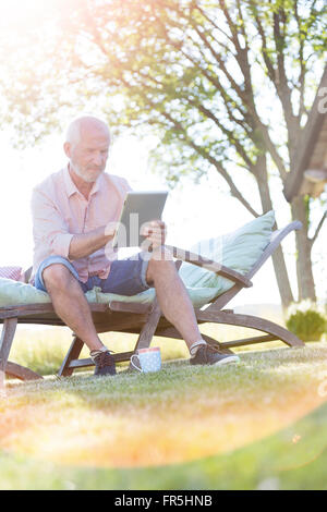 Senior man using digital tablet on lounge chair in backyard Stock Photo