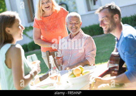 Family drinking wine and playing guitar at sunny patio table Stock Photo