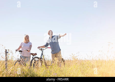 Senior couple bike riding in sunny rural field under blue sky Stock Photo