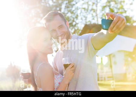 Young couple with wine taking selfie in sunny backyard