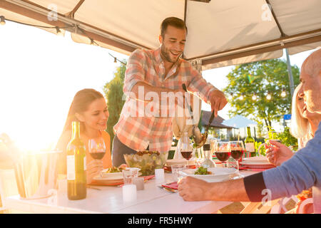 Man serving salad at sunny patio table Stock Photo